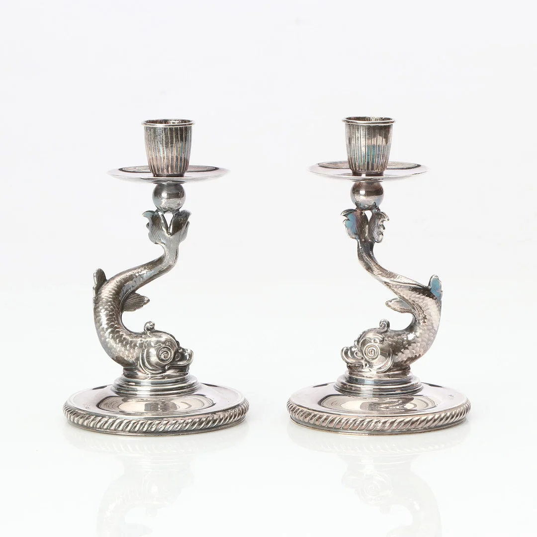 LJUSSTAKAR, ETT PAR. Silver. Dekor av delfiner. 1900-tal. Basplattor i annan metall. — Silver — Skånes Auktionsverk