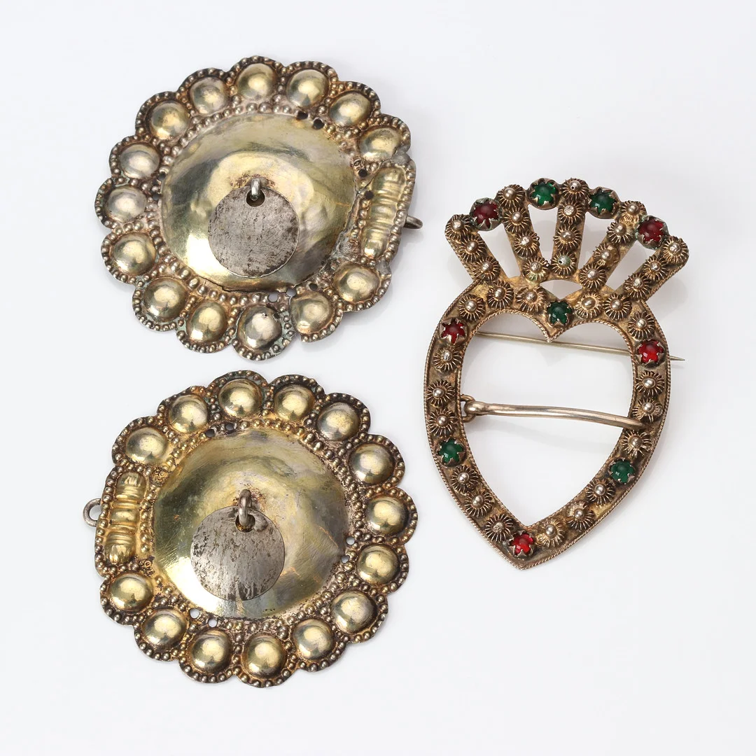 DRÄKTSMYCKEN, TVÅ ST. Förgyllt silver, ett med röd och grön paste (glas). — Brooches & Pendants — Skånes Auktionsverk