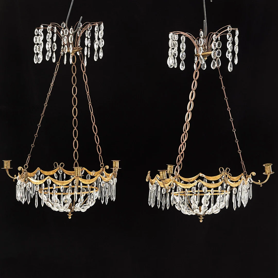 AMPLAR, 1 par, 1900-tal, empirestil, för 3+1 ljus, stomme i mässing, dekor av bokhuvuden, behängd med prismor. — Chandeliers — Stockholms Auktionsverk Magasin 5