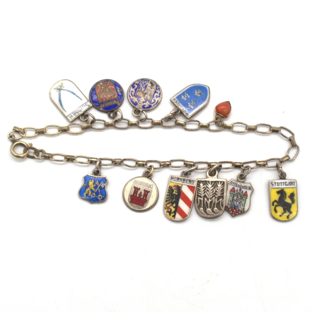 ANTIKES BETTELARMBAND AUS GOLD DOUBLE MIT ZEHN STÄDTEWAPPEN, ÜBERWIEGEND AUS SILBER, SOWIE EINEM HERZ ANHÄNGER AUS 8 KARAT GOLD MIT KORALLE CA. 19CM, UM CA. 1930. — Bracelets — Kunst- und Auktionshaus Kleinhenz