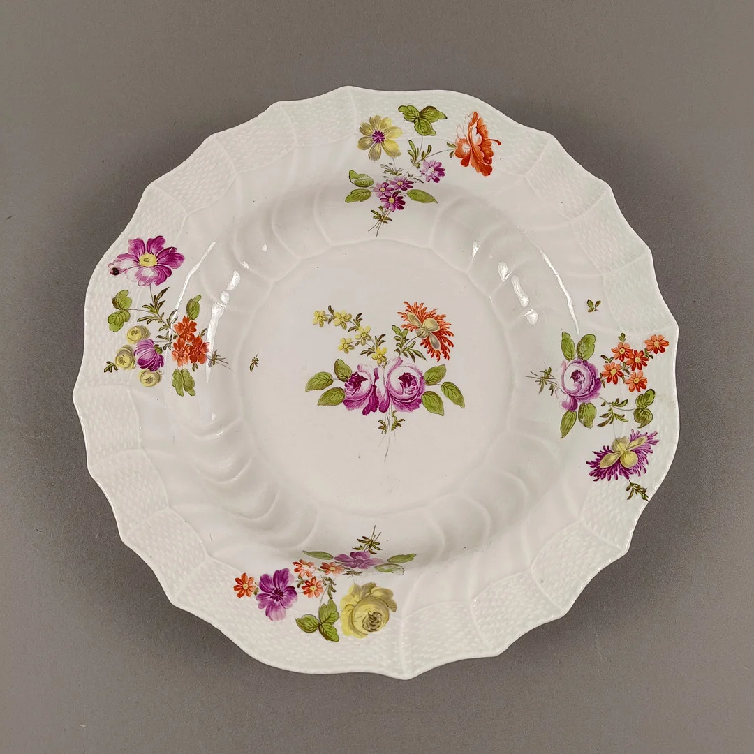 TELLER MIT BLUMENMALEREI - tief gemuldeter Rundteller, Porzellan, reliefierter Flechtrand. — European — Auktionshaus Blank