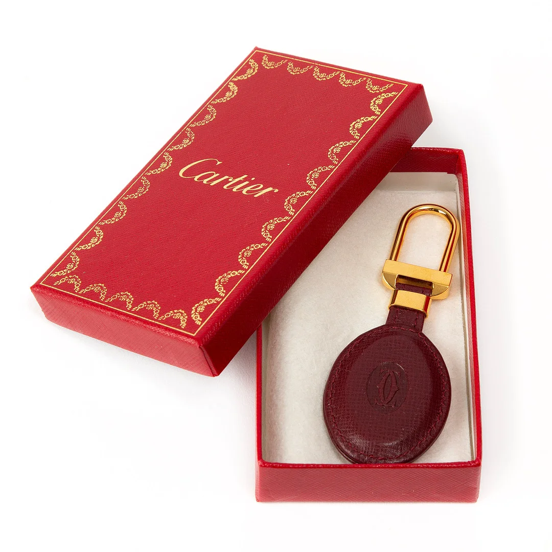 CARTIER. Nyckelring, vinrött läder och guldfärgad metall. — Vintage & Designer Fashion — Stockholms Auktionsverk Göteborg