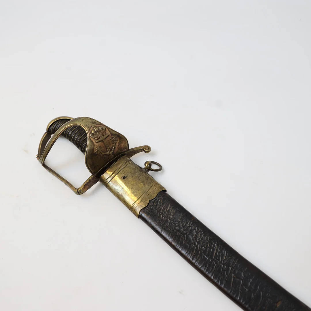 SJÖOFFICERSSABEL Svensk m/1780 med balja av läder och mässing. Parerskydd av mässing med flottans märke, Lindat handtag. — Edged weapons — Falun Auktionsbyrå