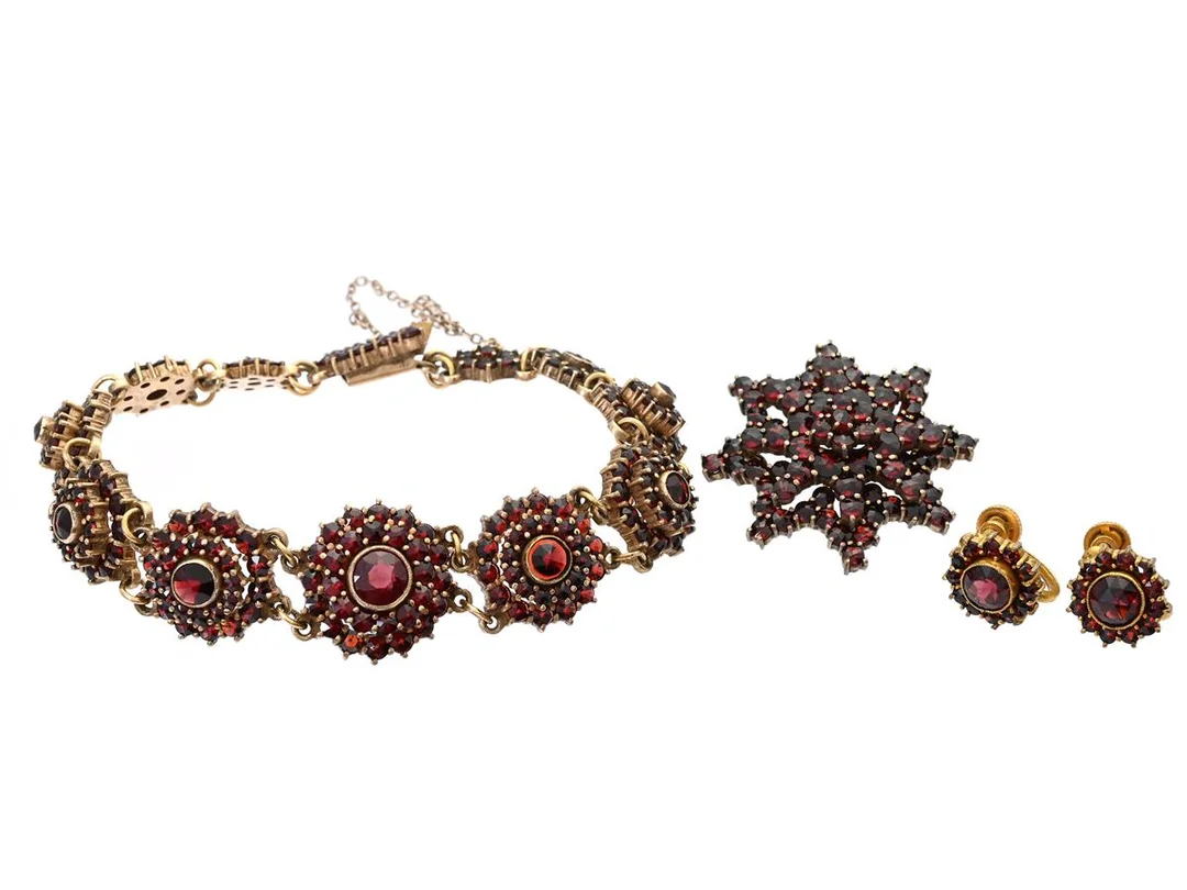 SMYCKESET, örhängen, brosch och armband, gulmetall, granater, örhängen höjd 12 mm, brosch diameter ca 30 mm, armband längd 18 cm,lvikt 29,3 g, örhängen med skruvmekanism, armband saknar en sten nära låset och har någon sten med mindre nagg. — Smycken/Smyckeset — Kaplans