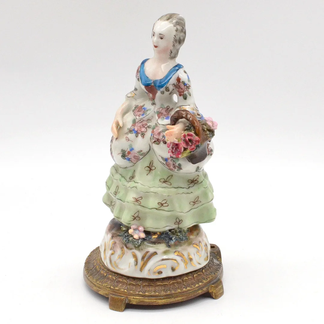 "FRAU MIT BLUMENKORB", FRANZÖSISCHE TAFELDEKORATION AUS PORZELLAN, POLYCHROM MIT GOLDMALEREI, AUF BRONZESOCKEL MONTIERT, UM 1850. — European — Kunst- und Auktionshaus Kleinhenz