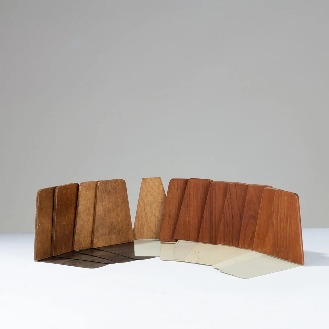 DANSK DESIGN: 12 assorterede bogstøtter af teakfinér og egetræ på metalfødder, Danmark, 1950'erne, (12). — Miscellaneous — Palsgaard Kunstauktioner