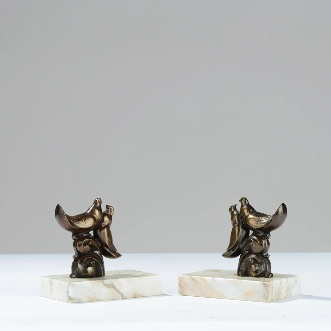 ART DECO: Et par bogstøtter med fugle af bronzepatineret metal på lyse marmorsokler, europæisk formgiver, 1900-tallets midte, (2). — Sculptures & Bronzes — Palsgaard Kunstauktioner