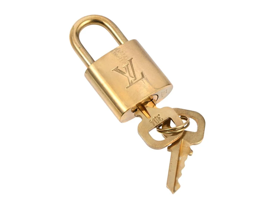 HÄNGLÅS, LOUIS VUITTON, guldfärgad metall, lås, två nycklar, nr 304. — Accessoarer/Övrigt — Kaplans