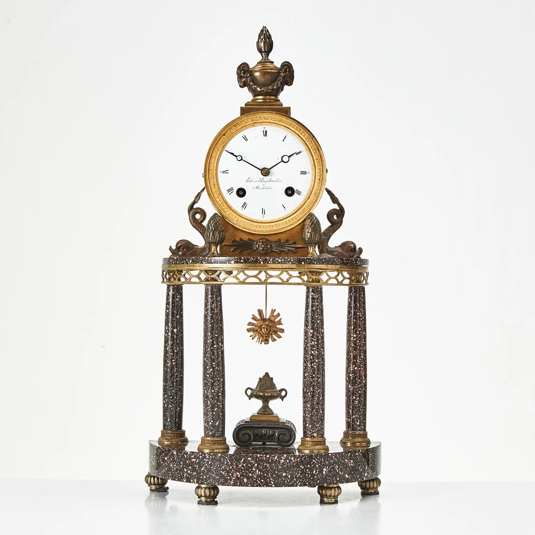 BORDSPENDYL så kallad "Pendule portique", sengustaviansk-stil med äldre delar, urtavlan signerad Eduard Engelbrechten Stockholm (urmakare verksam i Stockholm 1815-1845), Blybergsporfyr från Älvdalens Porfyrverk. — Mantel clocks — Stockholms Auktionsverk Magasin 5