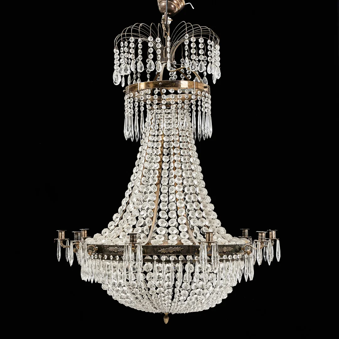 LJUSKRONA, 1900-talets andra hälft, empirestil, för 11 ljus, stomme i mässing, behängd med prismor, elektrifierad. — Chandeliers — Stockholms Auktionsverk Magasin 5