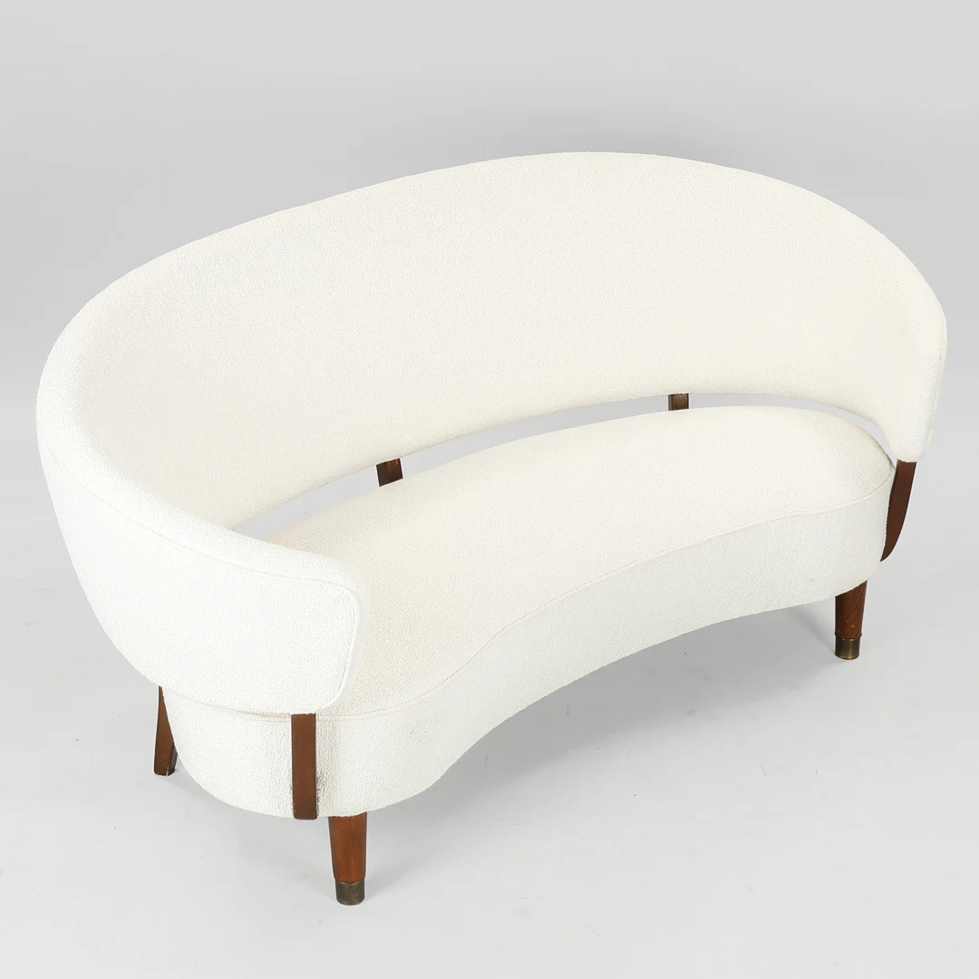 AAGE SATTRUP. Svungen sofa betrukket med hvid bouclé, stel og ben af bøg, forben med sko af messing, Sattrups Polstermøbelfabrik, Danmark, 1950'erne. — Sofas & Seatings — Palsgaard Kunstauktioner